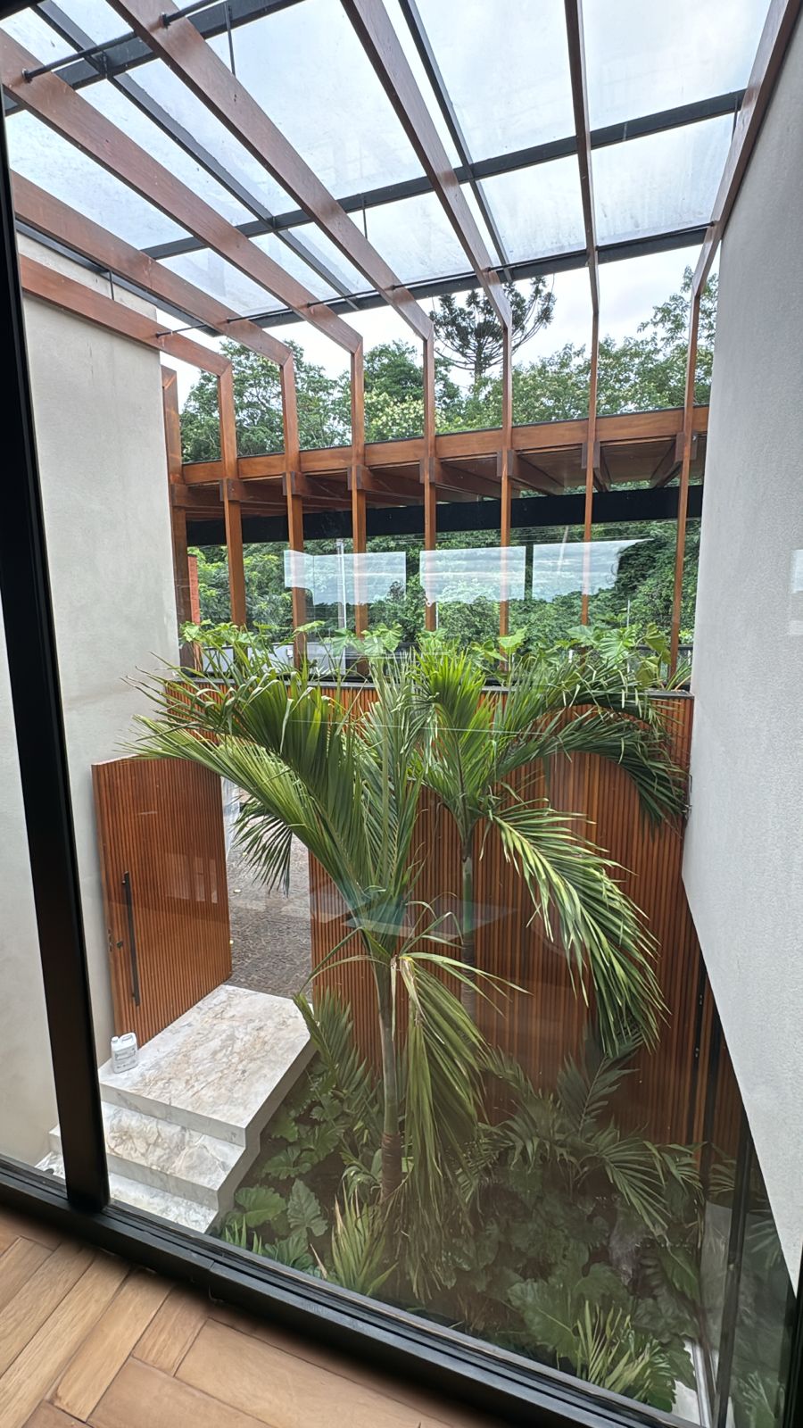 Área externa com pergolado, painéis ripados e portão pivotante em madeira, vistos do interior da residência — obra atendida pela Prado Marcenaria